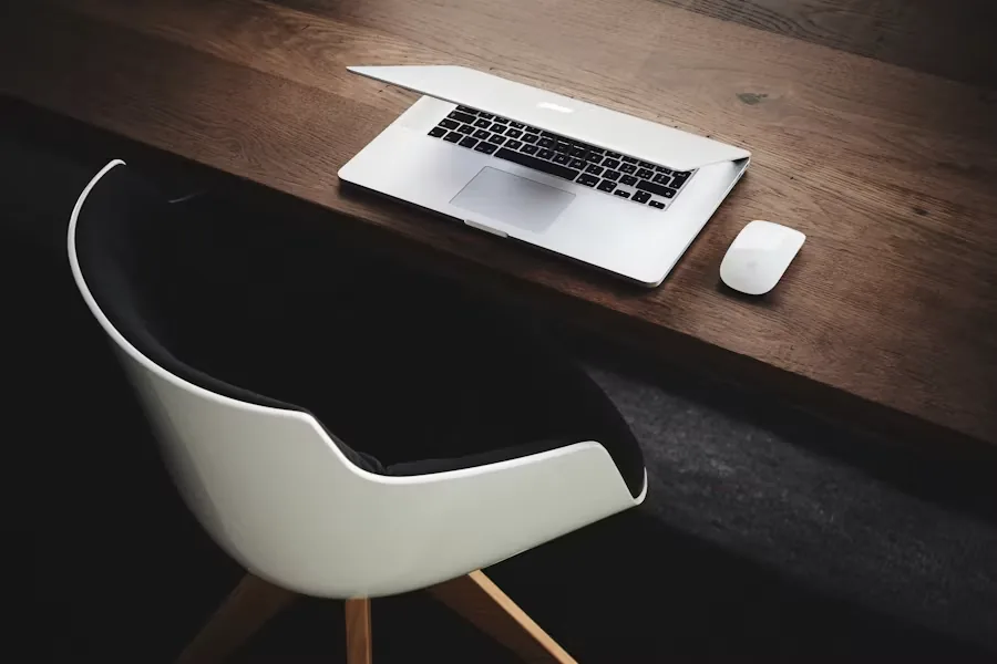 A laptop and mouse on a wooden desk beside an office chair